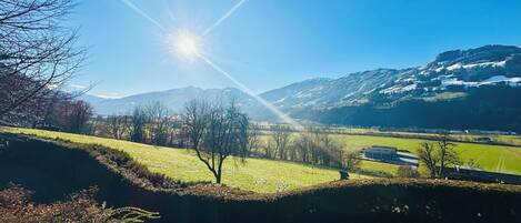 Un paysage rural avec un ciel dégagé, un soleil brillant et des montagnes en arrière-plan.