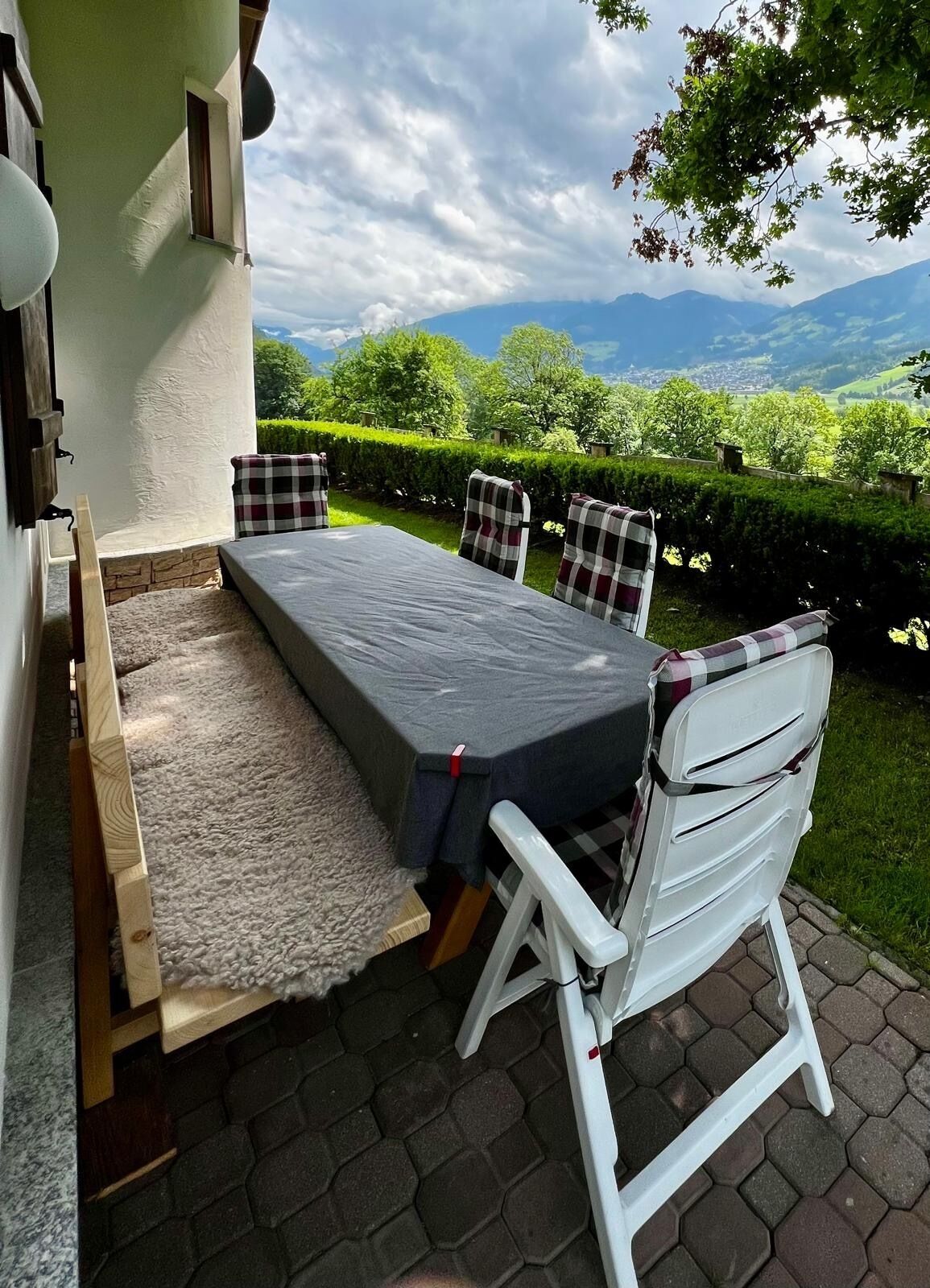 Une terrasse extérieure avec une table et des chaises, une vue sur des collines verdoyantes et des montagnes, et un bâtiment blanc avec une fenêtre.