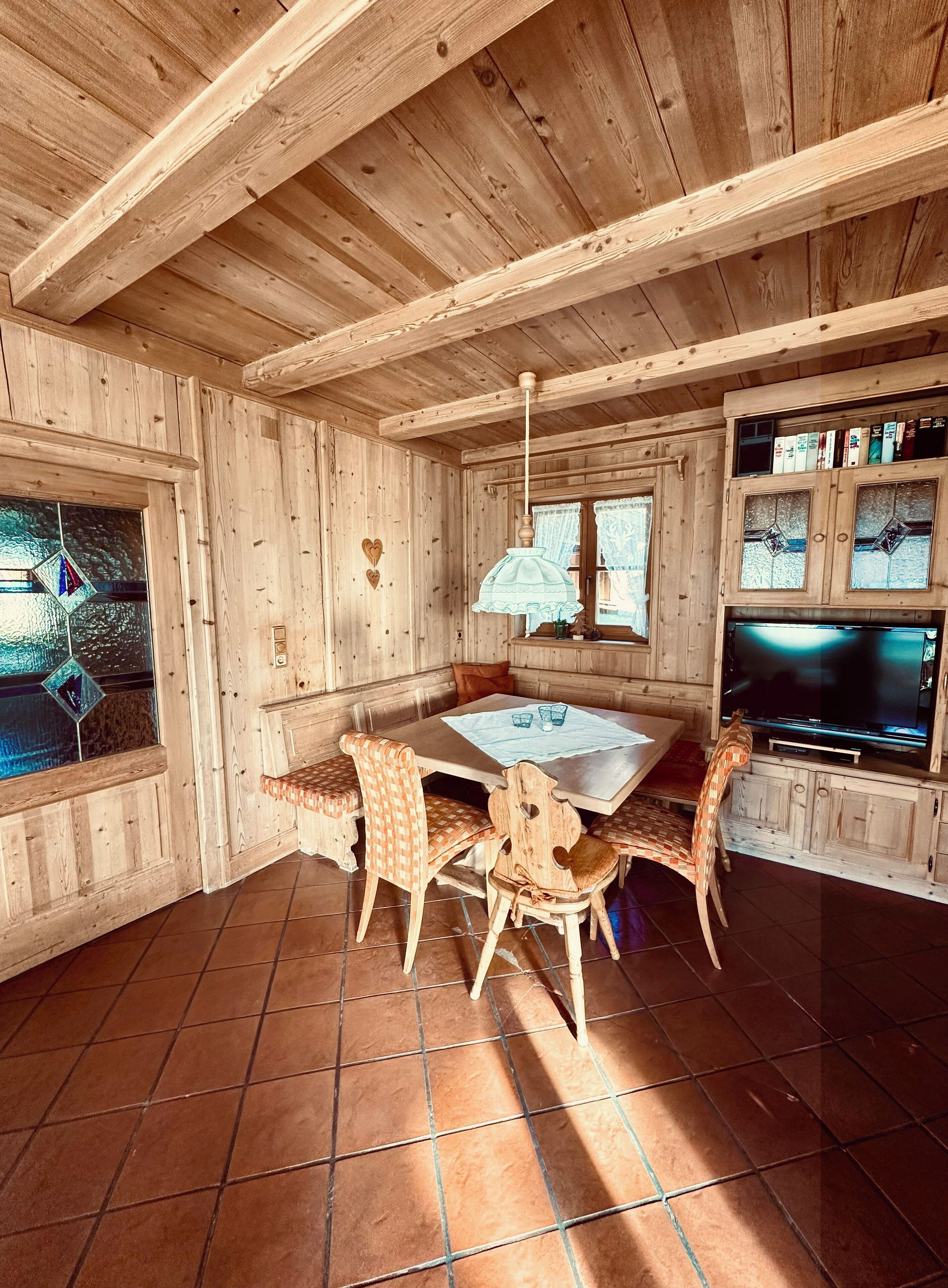 En inredning med träpanel, ett matbord, stolar, en tv och ett fönster med gardiner.