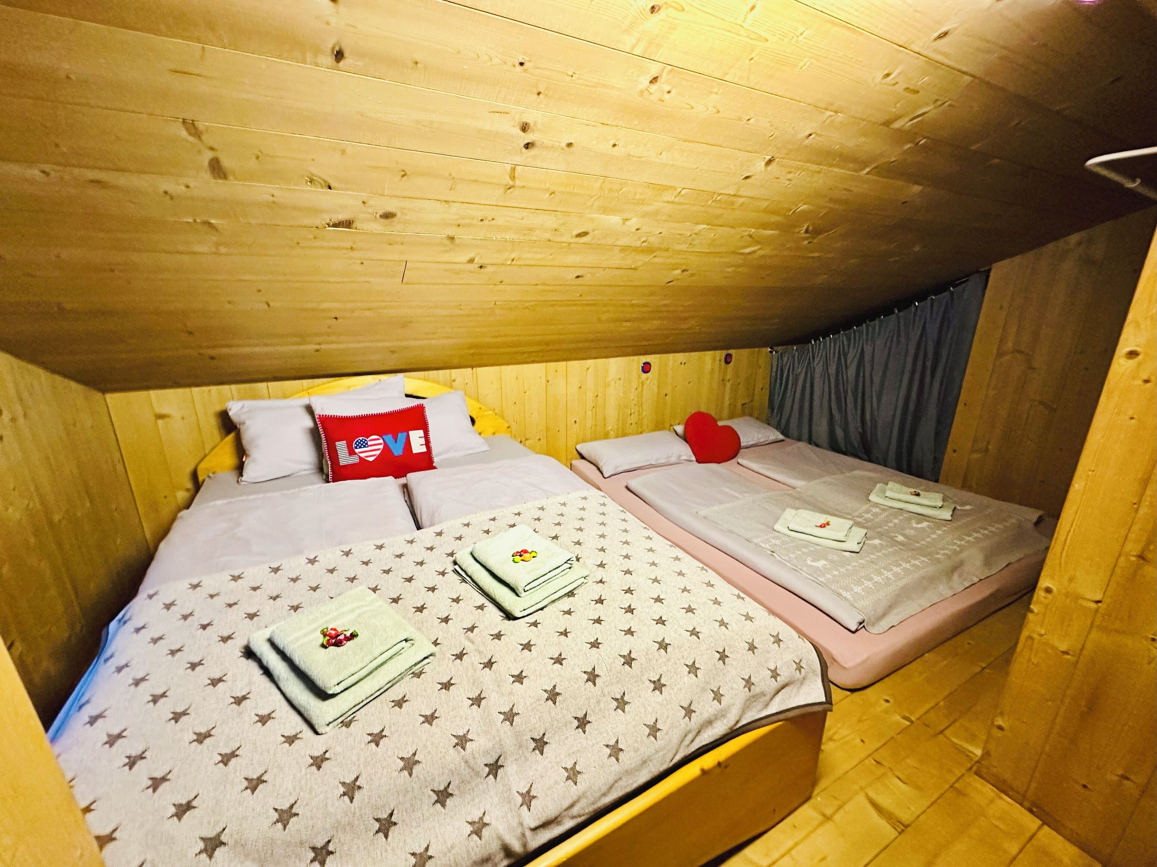 A wooden cabin room with two beds, each with star-patterned bedding and pillows, including a red pillow with 'LOVE' and an American flag design.