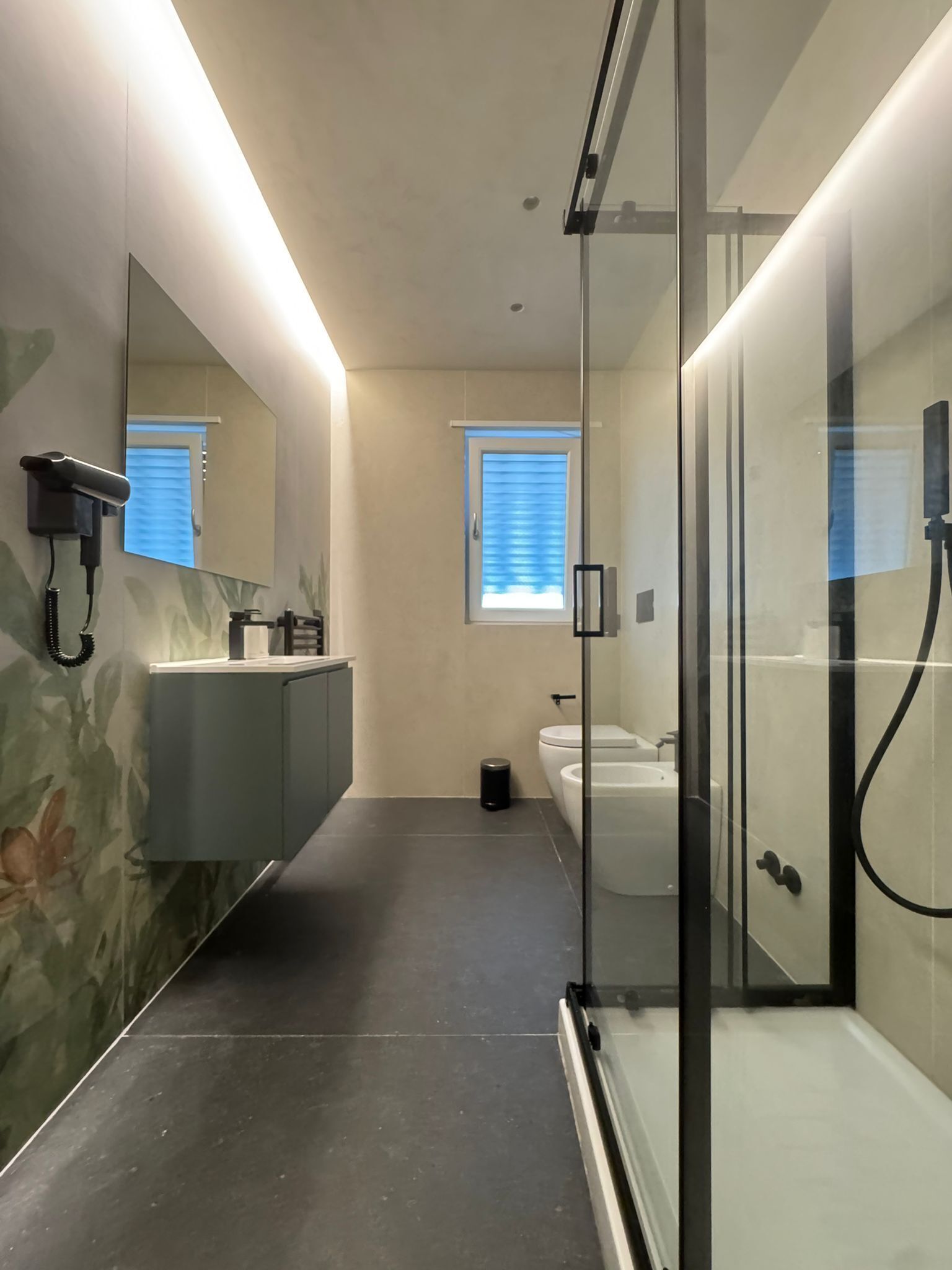 Ein modernes Badezimmer mit einer Duschkabine, einem großen Spiegel und einem WC mit Fenster darüber.