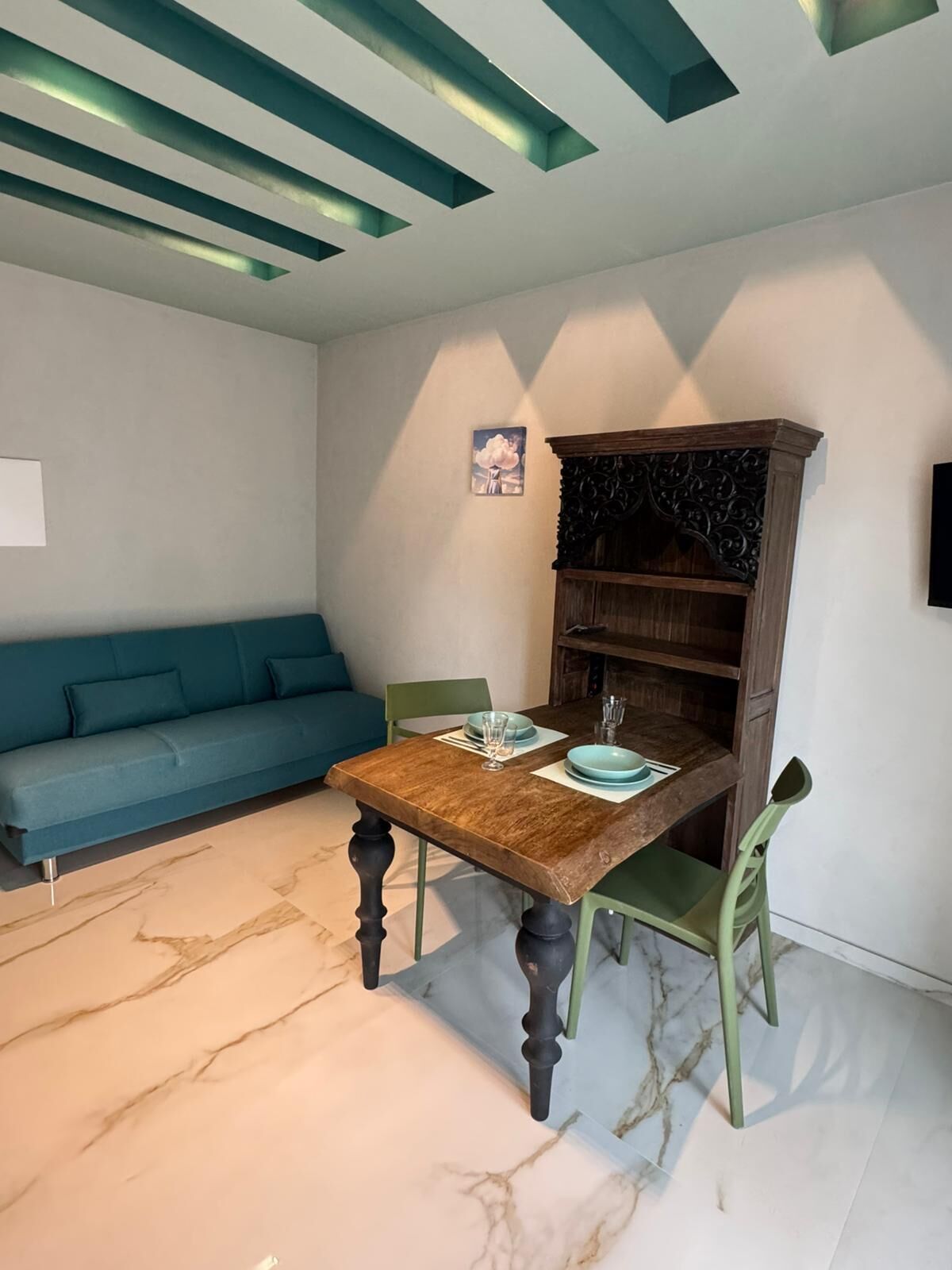 A dining area with a wooden table and chairs, a blue sofa, and a wooden bookshelf.