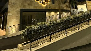 A modern building with a geometric light pattern on the facade, a palm tree, and a staircase leading to the entrance. - Paradisea club and residences (Volla)