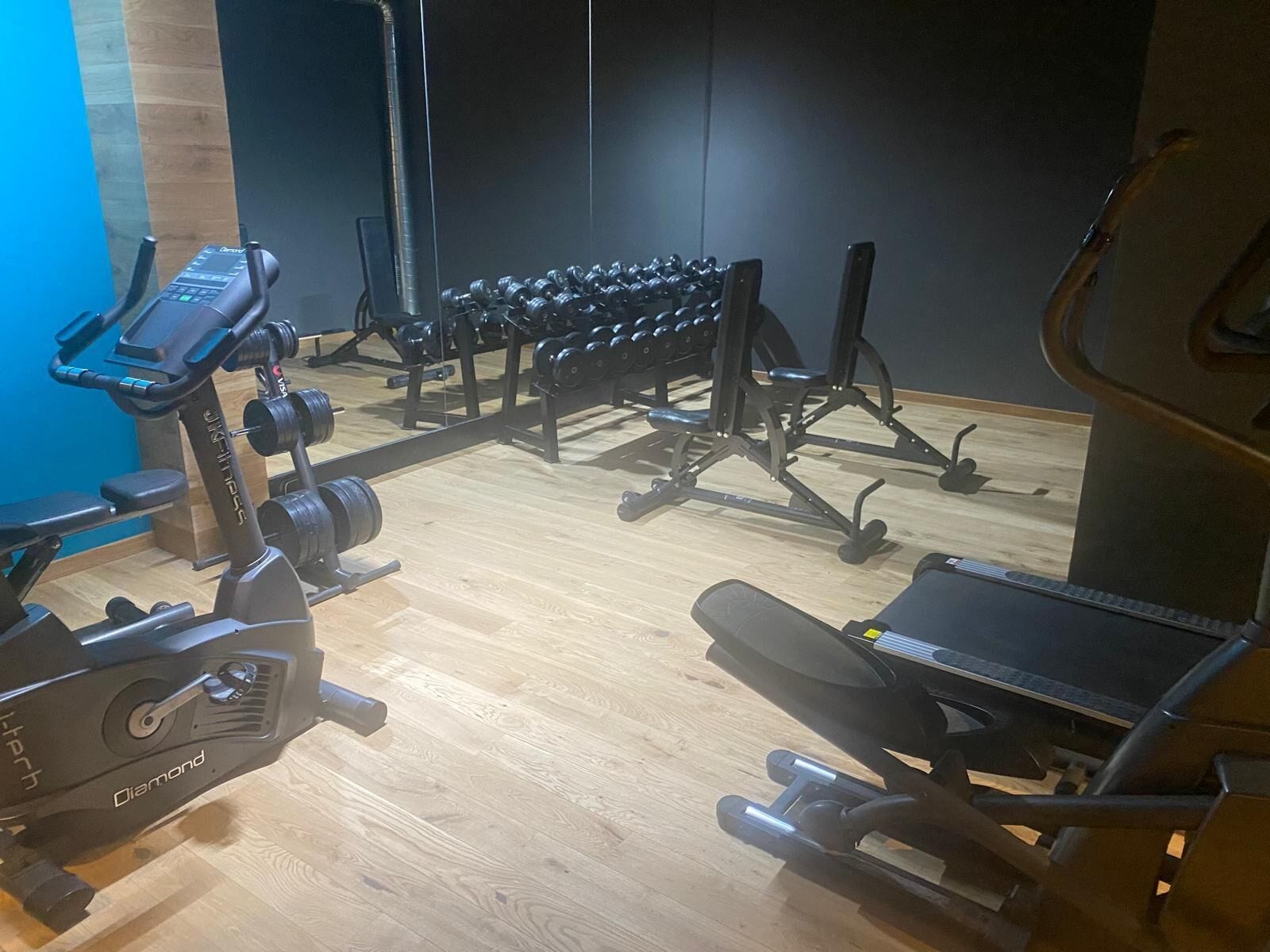 Un gimnasio con diversos equipos de ejercicio, incluyendo una cinta de correr, banco de pesas y mancuernas.