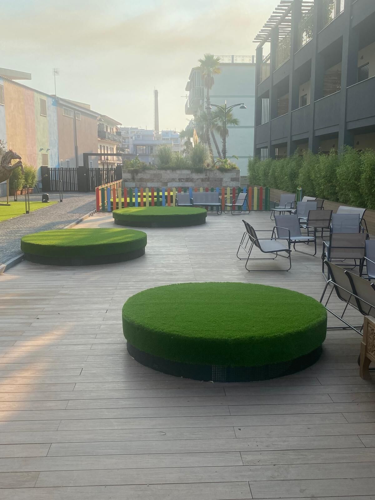 Une cour intérieure agrémentée de jardinières rondes et verdoyantes, d’un espace de détente extérieur et offrant une vue sur les bâtiments en arrière-plan.
