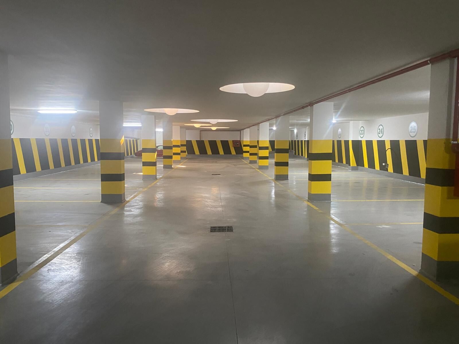 A multi-level parking garage with yellow and black striped pillars, clear ceiling lights, and numbered parking spots.
