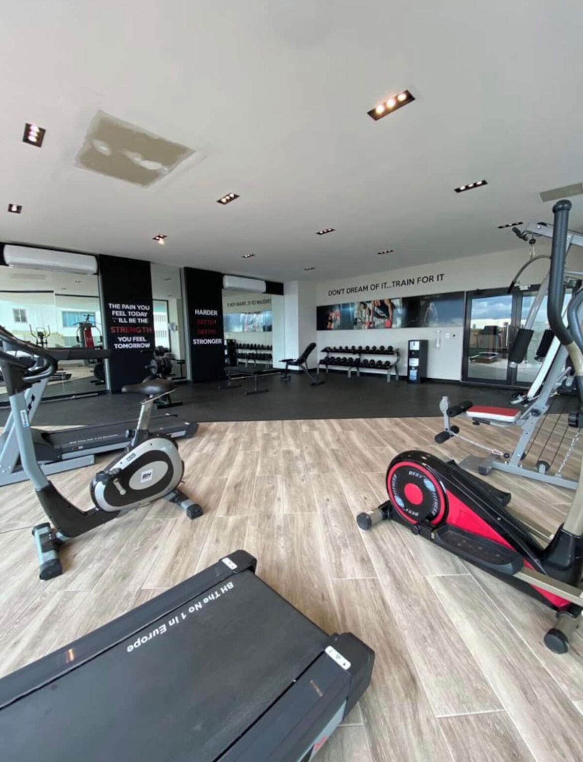 A modern gym with treadmills, elliptical machines, and free weights.