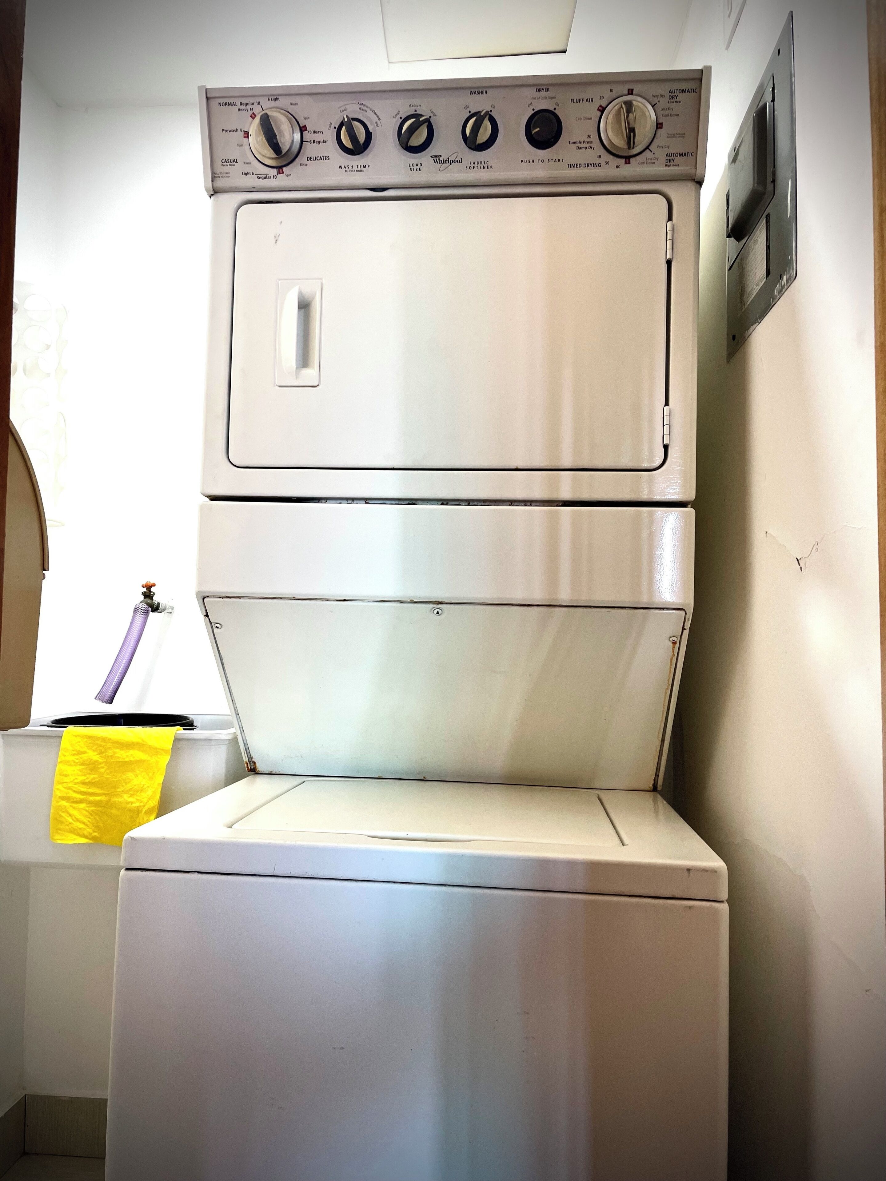 A front-loading washer and dryer unit with control knobs and a yellow cloth hanging nearby.