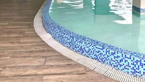 Piscina amb un videt de rajola, sòl de fusta i zona de seients amb cadires i taules.