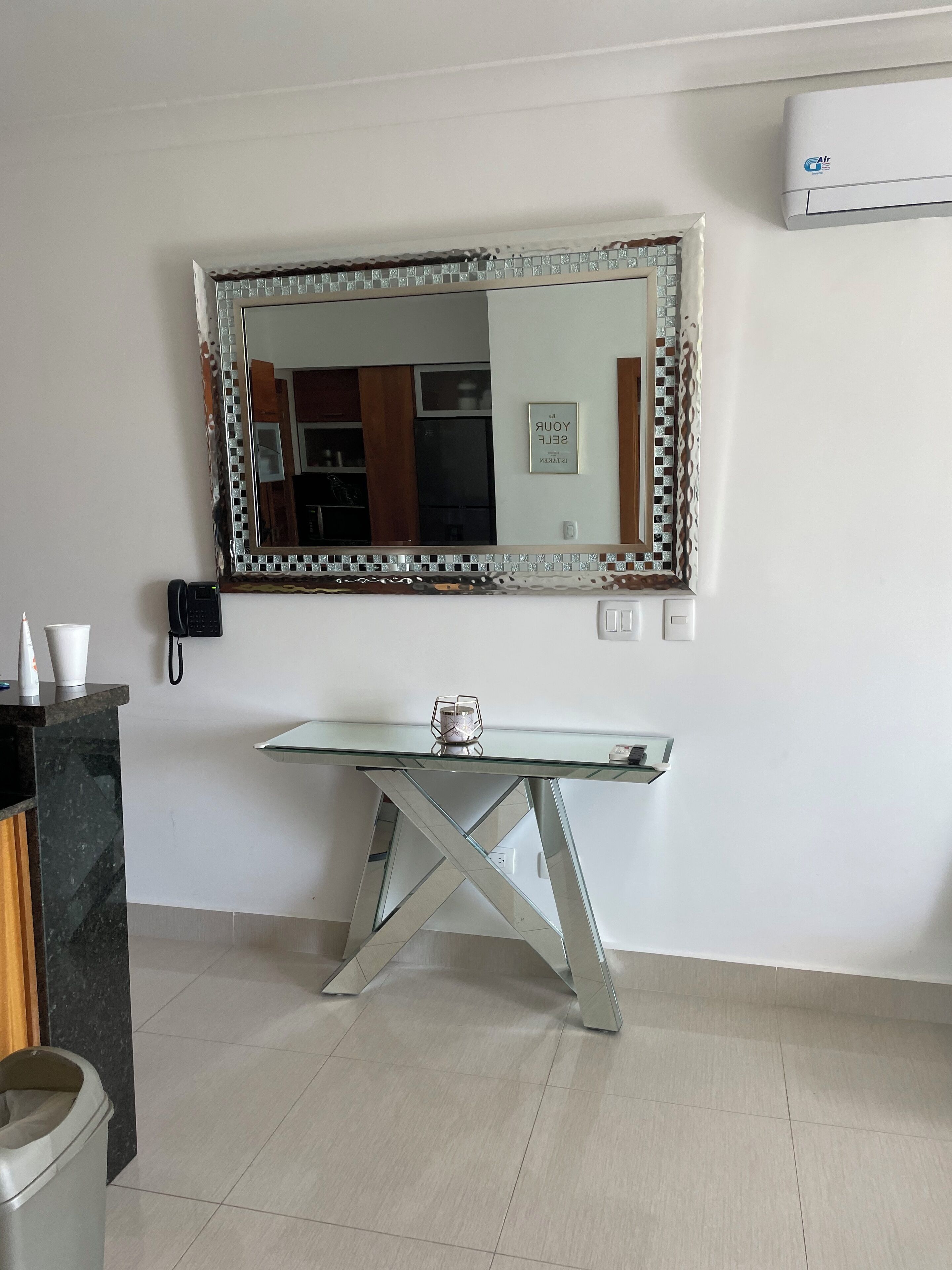A modern bathroom with a large mirror, a glass-top vanity, a black telephone, and a trash bin.