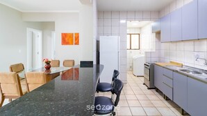A modern kitchen with grey cabinets, a black countertop, and a dining area with a glass table and chairs. - Fully Equipped Apartments in Meia Praia, 150m From the sea - Eoos (Itapema)