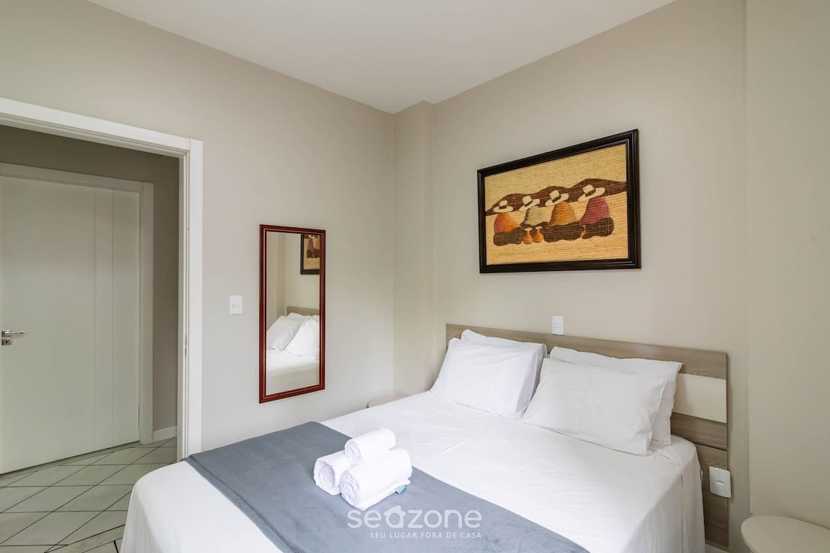 Quarto de hotel com uma cama, um espelho, um quadro e uma toalha sobre a cama.