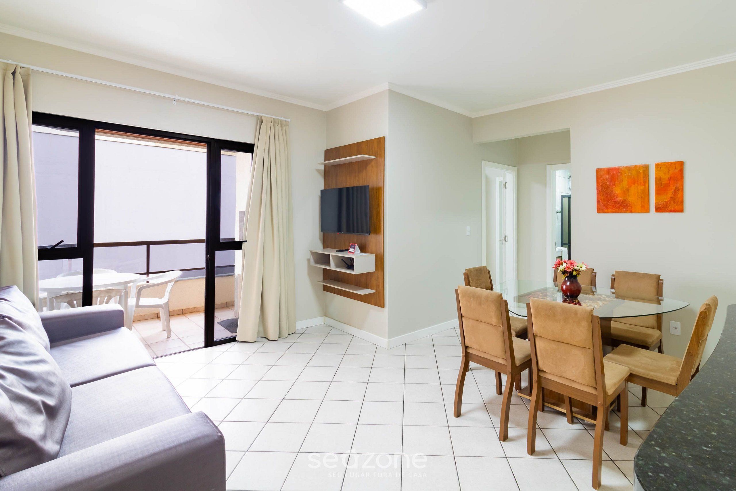 Una sala de estar moderna con un sofá, una mesa de comedor con sillas, un televisor montado en la pared y un balcón con vistas.
