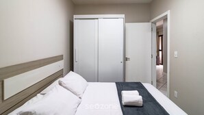 A bedroom with a bed, a wardrobe, and a door leading to another room. - Fully Equipped Apartments in Meia Praia, 150m From the sea - Eoos (Itapema)