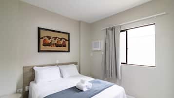 Quarto de hotel com cama, quadro na parede, aparelho de ar condicionado e janela com cortinas.