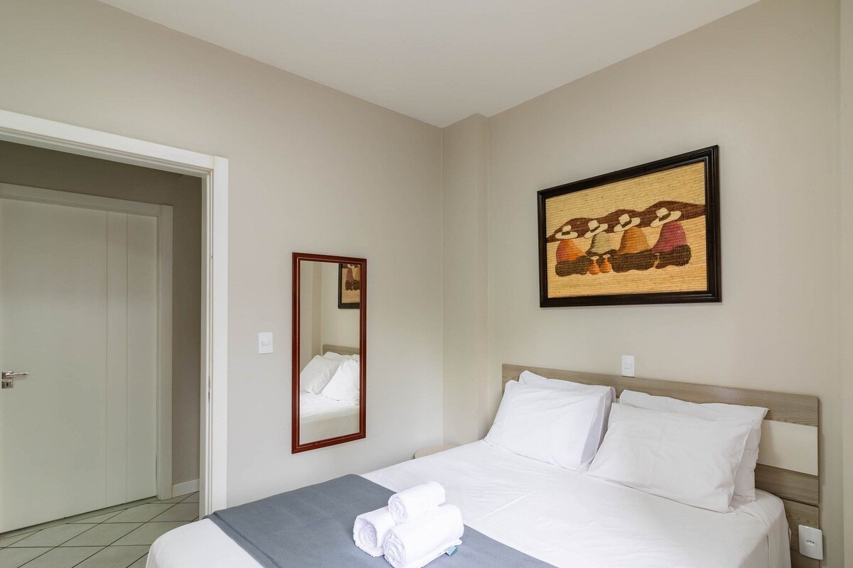 A hotel room with a bed, a mirror, a painting, and a towel on the bed.