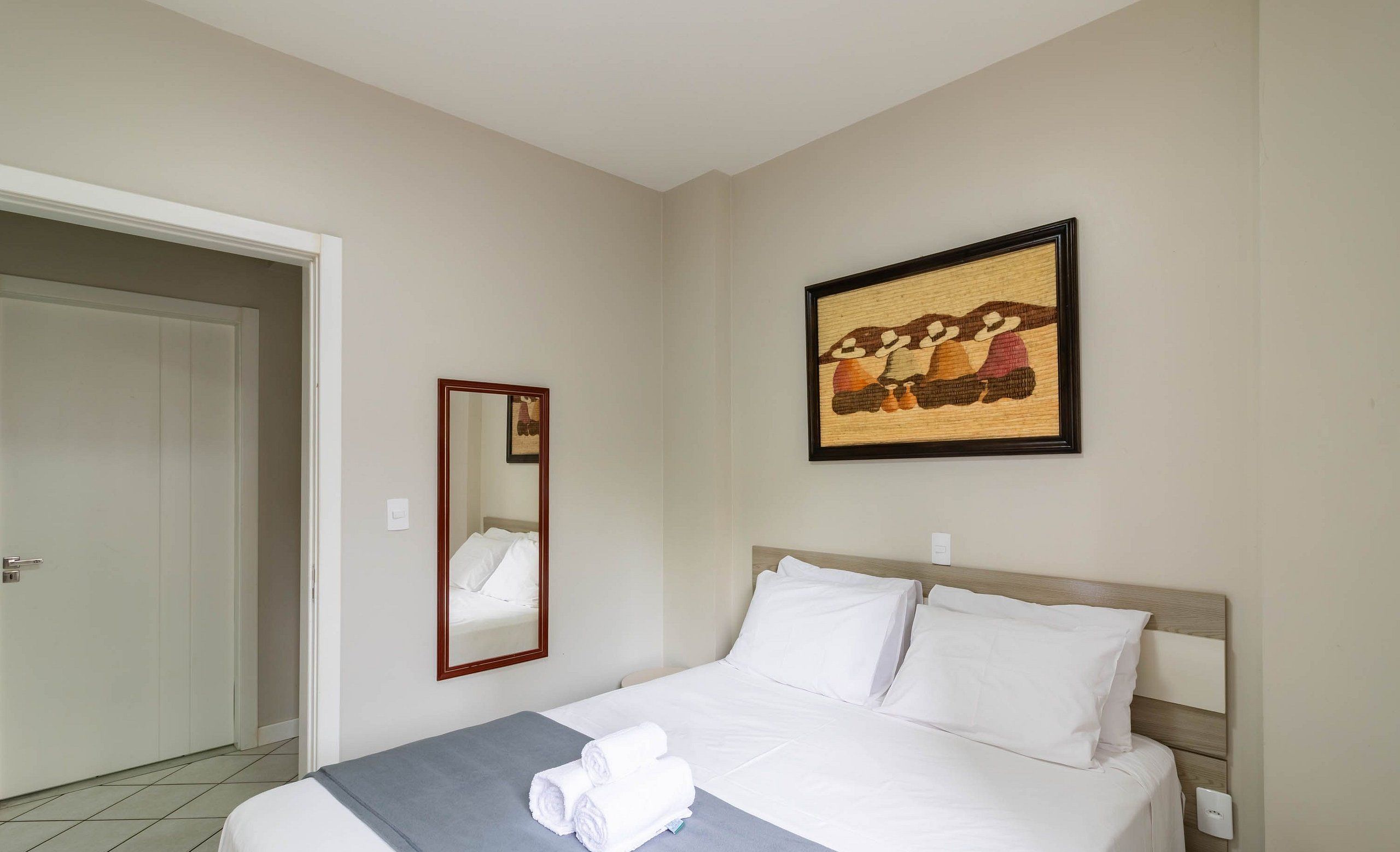 Habitación de hotel con cama, espejo, un cuadro y una toalla sobre la cama.