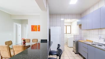 Uma cozinha moderna com armários cinza, bancada preta e área de jantar com mesa e cadeiras de vidro.