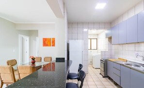 A modern kitchen with grey cabinets, a black countertop, and a dining area with a glass table and chairs. - Fully Equipped Apartments in Meia Praia, 150m From the sea - Eoos (Itapema)