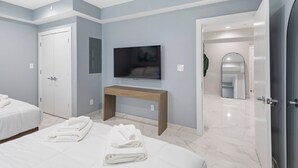 Et moderne hotelværelse med to senge, et fjernsyn, et træskab og et badeværelse, der kan ses igennem en åben dør.