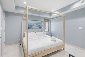 Ein modernes Schlafzimmer mit einem Himmelbett, einem Bild eines Piers und einem Fenster.