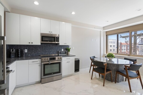 A modern kitchen with white cabinets, a built-in oven, a microwave, and a dining area with a table and chairs.