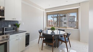 Une cuisine moderne avec coin repas, dotée d’un plan de travail en marbre, d’appareils électroménagers en acier inoxydable et offrant une vue sur la ville grâce à de grandes fenêtres.
