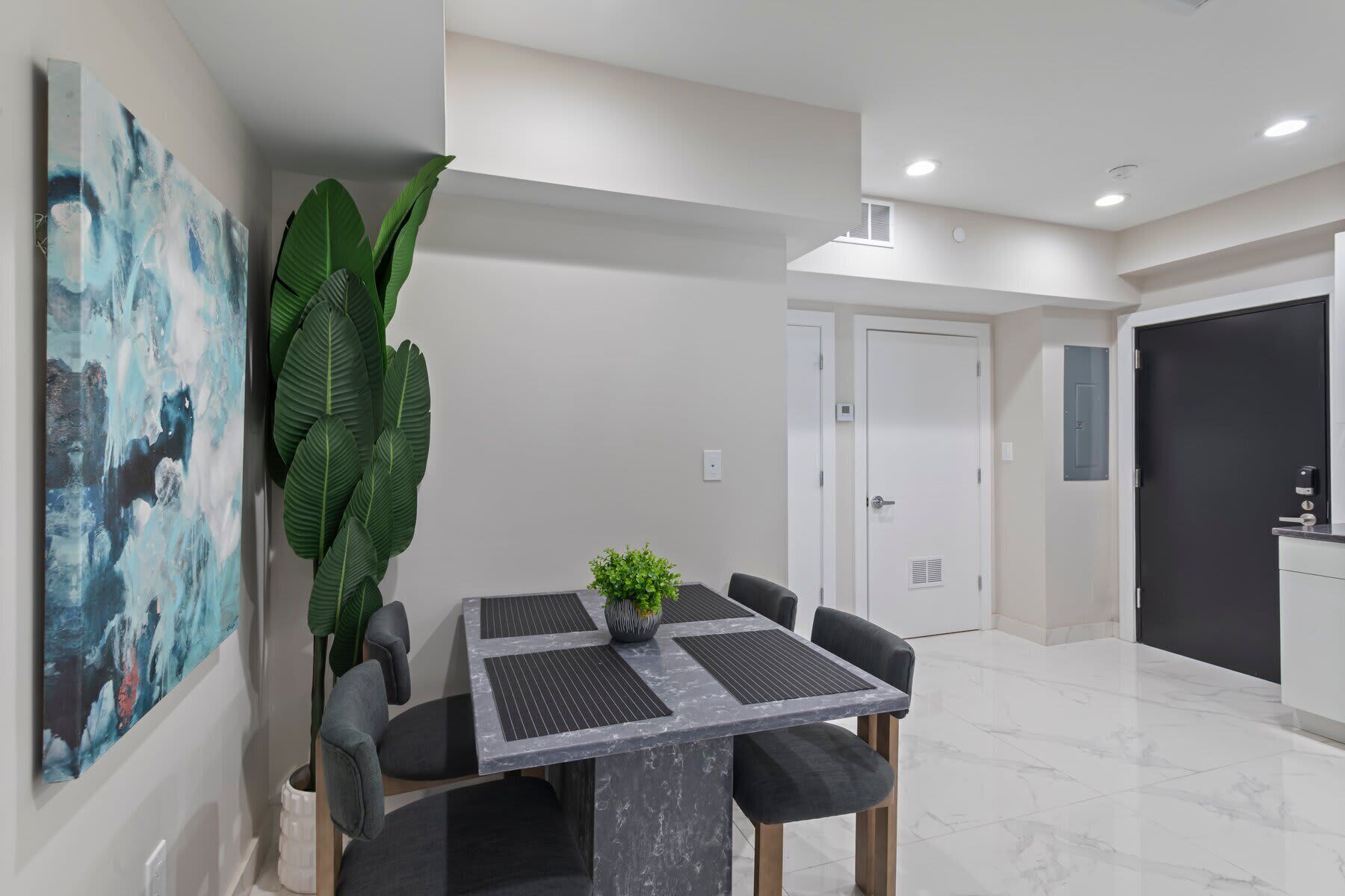 A modern dining area with a marble table, black chairs, and a potted plant.