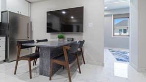 A modern kitchen with a marble countertop, a built-in refrigerator, and a flat-screen TV mounted above the island. - Ammos Luxury Living- Paros Suite (Ventnor City)