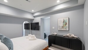 A modern bedroom with a bed, a flat-screen TV, a radiator, and artwork on the wall. - Ammos Luxury Living- Paros Suite (Ventnor City)