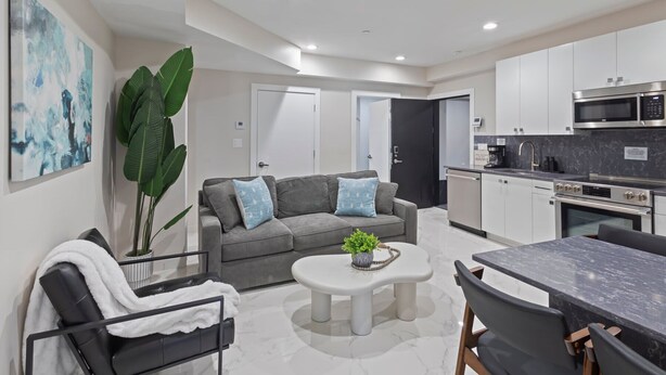 A modern apartment with a grey sofa, white coffee table, and a dining area with a marble table. - Ammos Luxury Living- Paros Suite (Ventnor City)