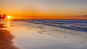 A beach at sunset with waves, a clear sky, and a distant building. - Ammos Luxury Living- Paros Suite (Ventnor City)