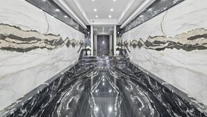 A modern hallway with marble walls and floors, leading to a door at the end.