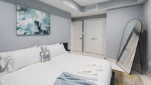 A modern bedroom with a large bed, a painting on the wall, a wardrobe, and a mirror.