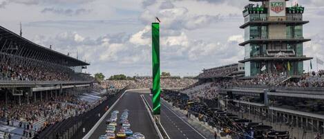 A race track with multiple cars lined up, a green flag, and a control tower.