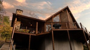 Une cabane en rondins à deux étages, dotée d’un balcon et d’une grande fenêtre.