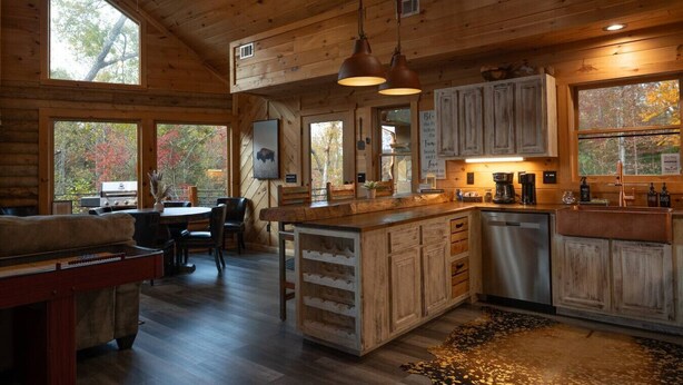 L’intérieur d’un chalet rustique comprend un coin repas, une cuisine et de grandes fenêtres.