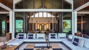 A spacious living area with a large sofa set, a coffee table, and a view of the interior through large glass doors. - Oceans 8 Villa 6BR (Sandy Bay)