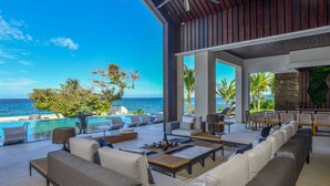 A spacious outdoor lounge area with a pool, seating, and a view of the ocean. - Oceans 8 Villa 6BR (Sandy Bay)