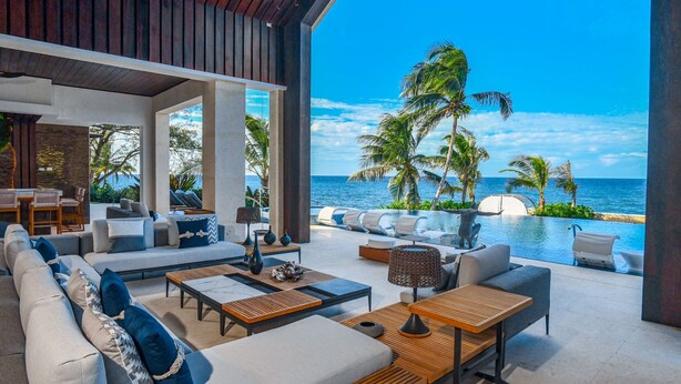 A modern outdoor lounge area with a pool, seating, and a view of the ocean. - Oceans 8 Villa 6BR (Sandy Bay)