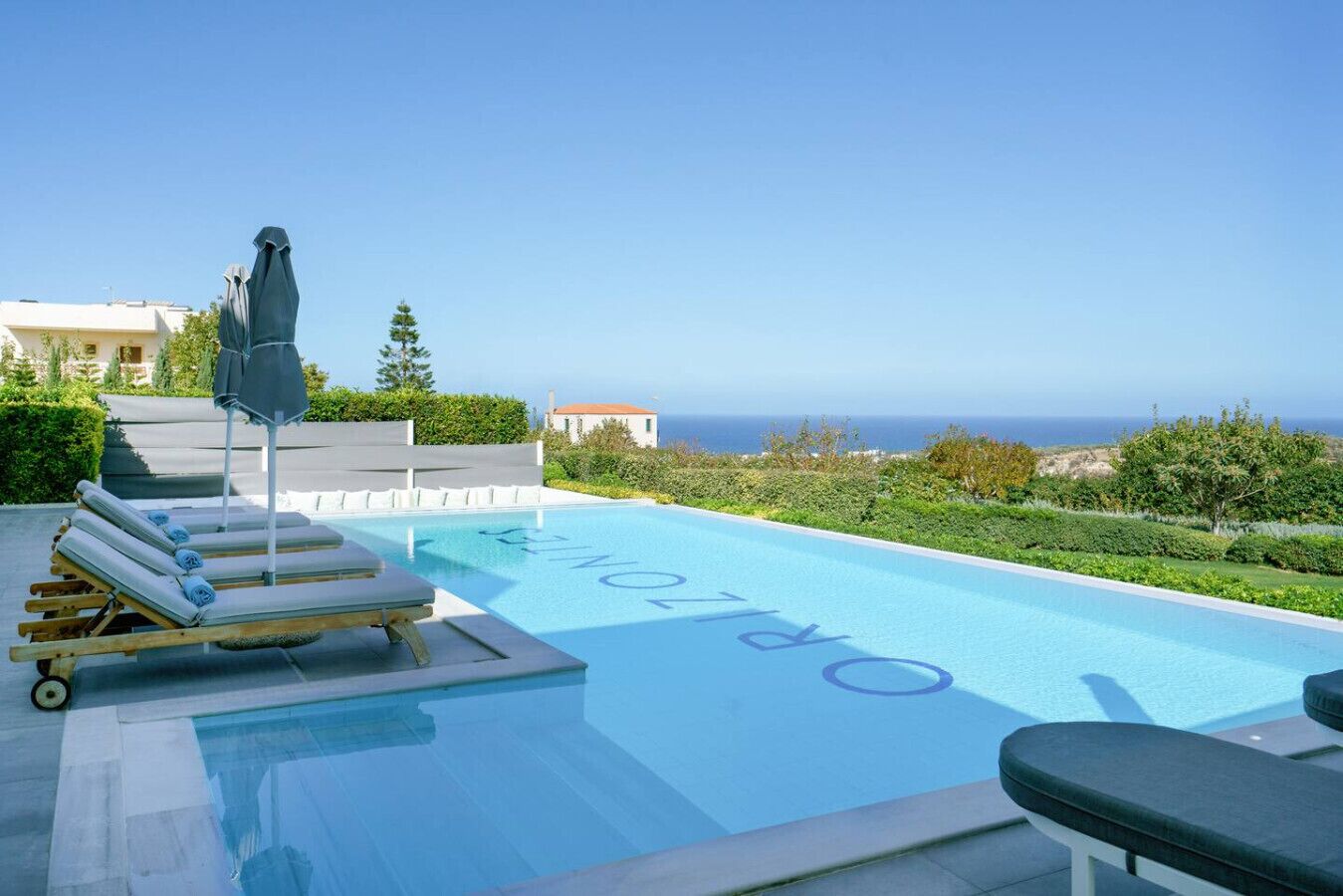 Piscina con sillones y sombrillas, cielo despejado y vista al mar.
