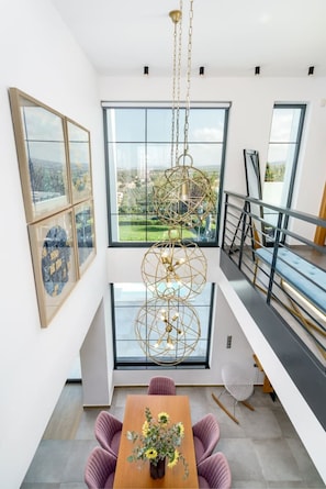 Ein modernes Interieur mit Essbereich, großen Fenstern und einer Hängeleuchte.