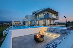 A modern two-story house with a swimming pool, outdoor seating, and a fire pit.