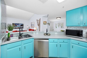 Een moderne keuken met blauwgroene kastjes, roestvrijstalen apparatuur en een betegelde spatwand.