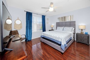 Ein Hotelzimmer mit Bett, Nachttischen, Schreibtisch, Stuhl, Deckenventilator und einem Fenster mit Vorhängen.