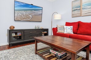 Ein Wohnzimmer mit einem Holztisch, einem roten Sofa, einem Bücherregal und einem großen Gemälde mit Strandmotiv an der Wand.