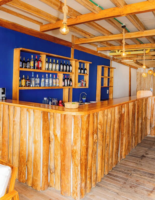 A wooden bar with shelves of bottles and glasses, a sink, and a wooden floor. - Mar Barú Beach House (Cartagena)