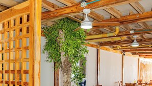 A wooden interior with tables and chairs, a ceiling fan, and a large tree. - Mar Barú Beach House (Cartagena)