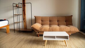 A room with a brown sofa, a white coffee table, a wooden bench, and a metal shelf unit against a wooden floor and white walls. - Mar Barú Beach House (Cartagena)
