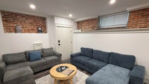 Un salon moderne avec deux canapés gris, une table basse en bois et un mur en briques.
